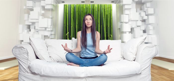 Young woman sitting on a sofa in the lotus position meditating i